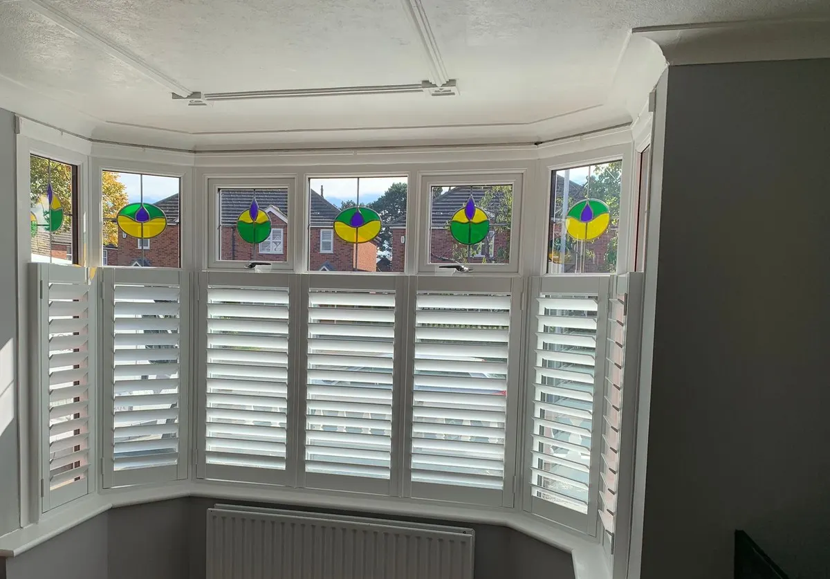 Café-style plantation shutters below stained glass top lights in a five-sided bay window