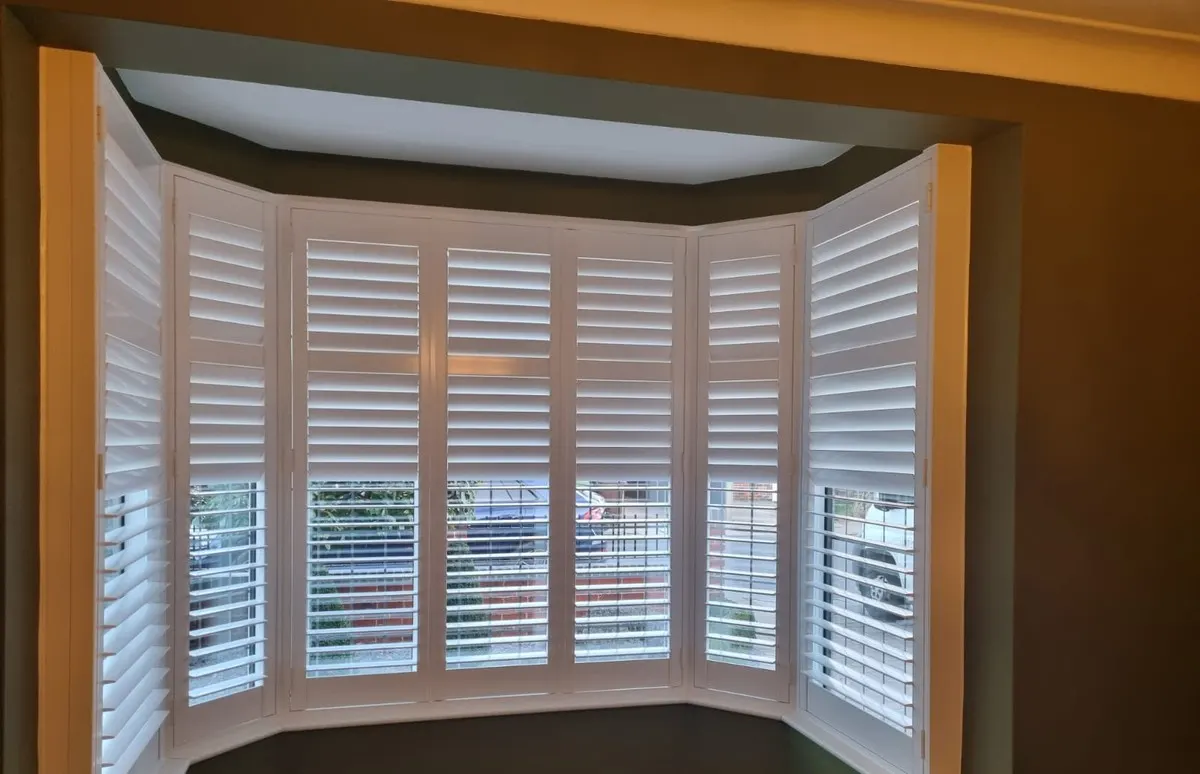 White plantation shutters fitted to a five-sided bay window with matching panels on each facet