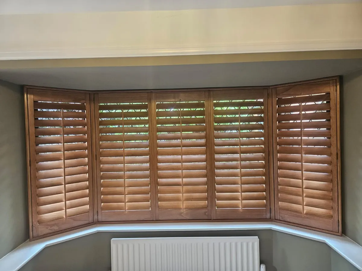 Wood-stained plantation shutters fitted across a three-sided splayed bay window in a living room