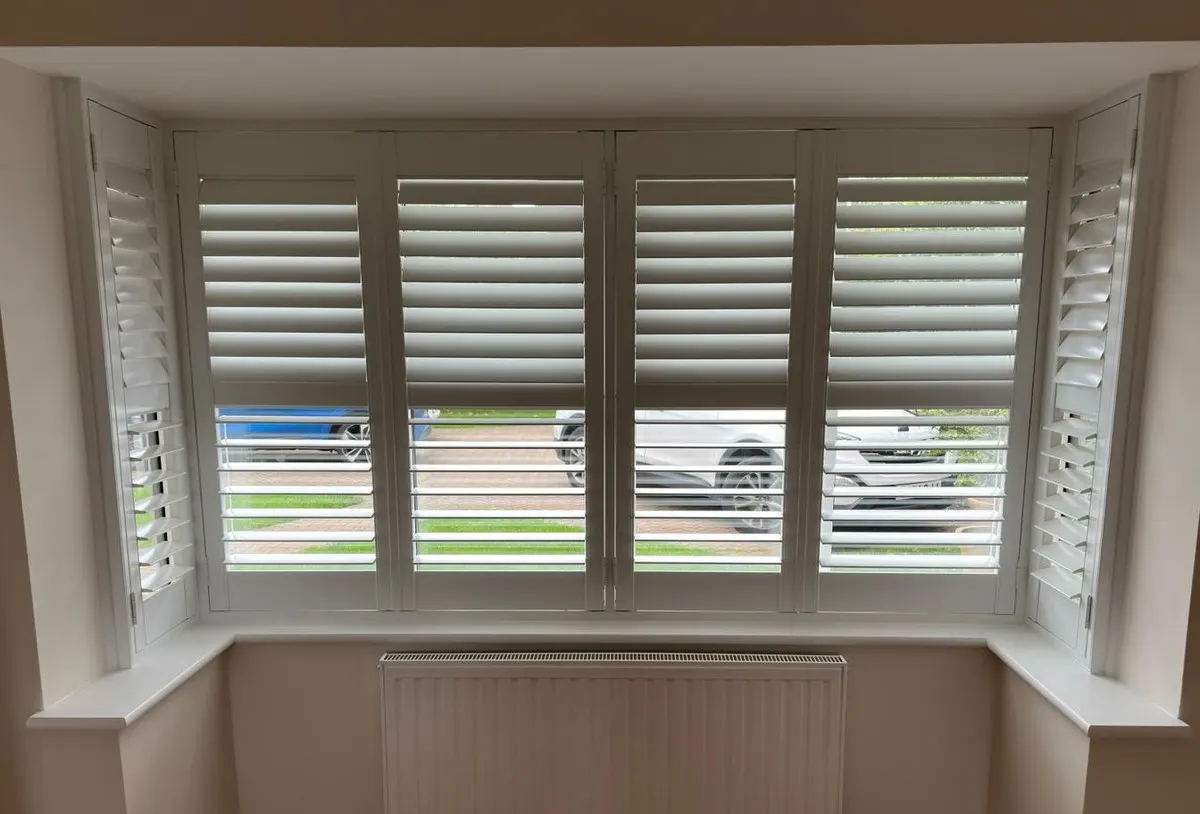 White full-height plantation shutters fitted to a square box bay window in a bright room