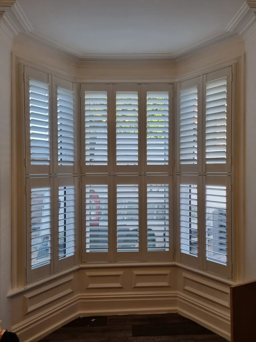 Cream tier-on-tier plantation shutters in a splayed bay window of a period property