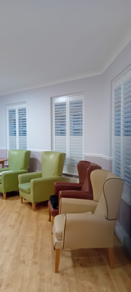 Wide view of a care home communal lounge with multiple shutter installations