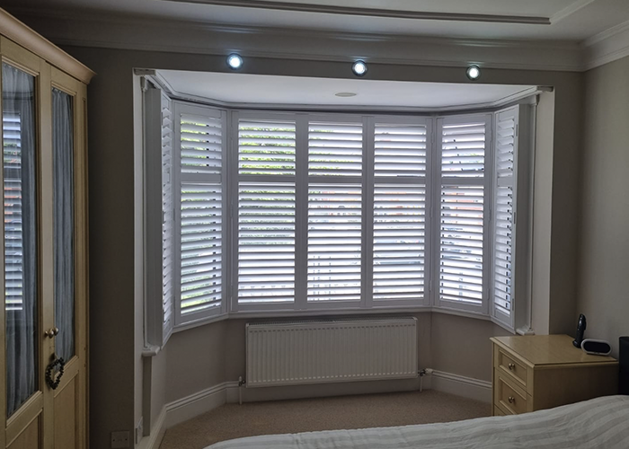 Worcester Shutters in the Bay Window of a modern bedroom, lit by spotlights