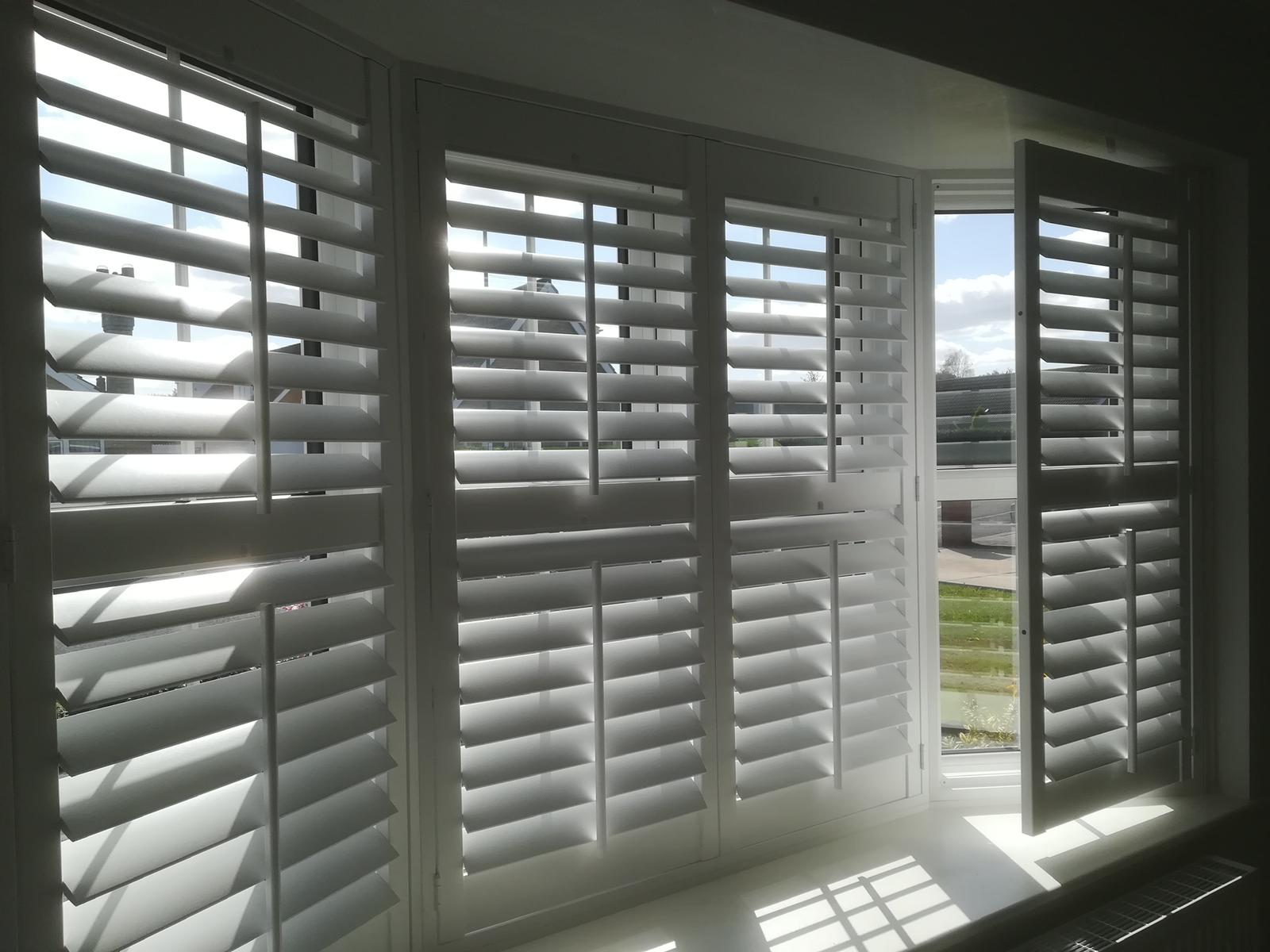 White plantation shutters on a bay window overlooking a garden