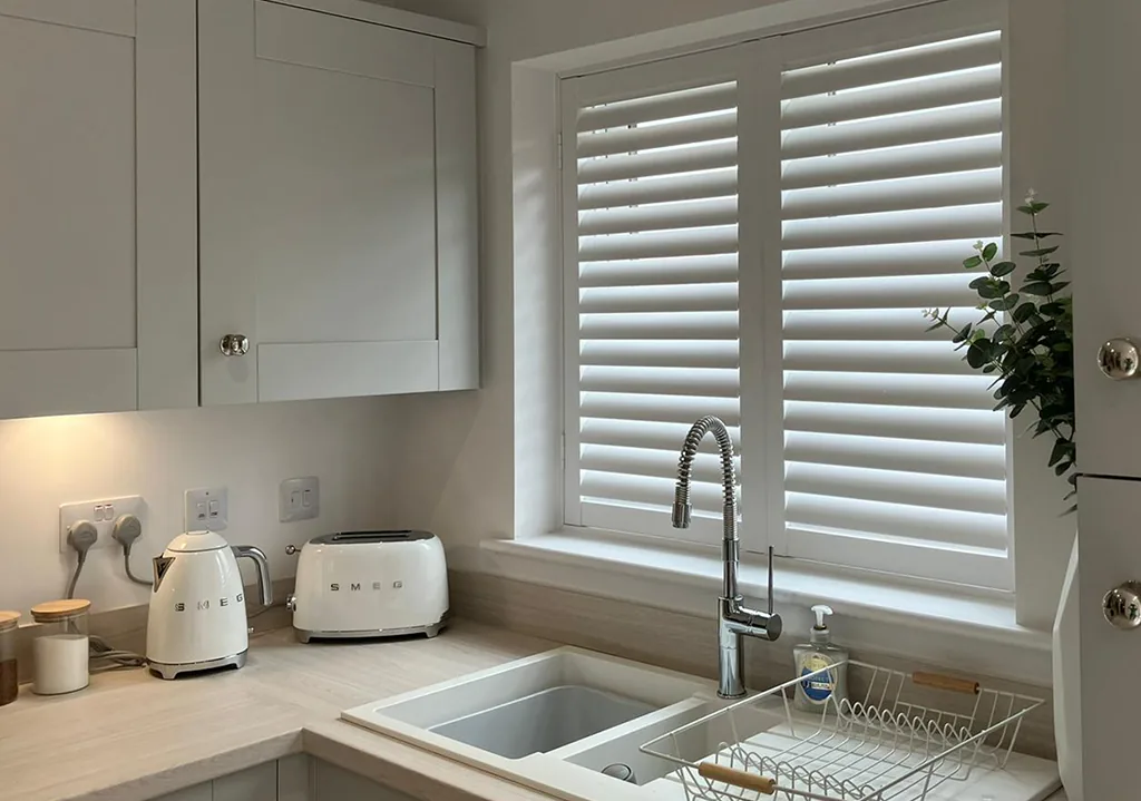 White plantation shutters fitted above a kitchen sink in a modern shaker kitchen