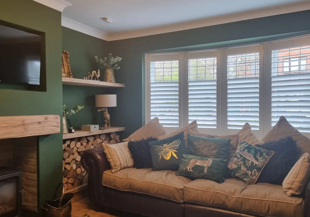 White plantation shutters in a bay window of a cosy living room with a green feature wall