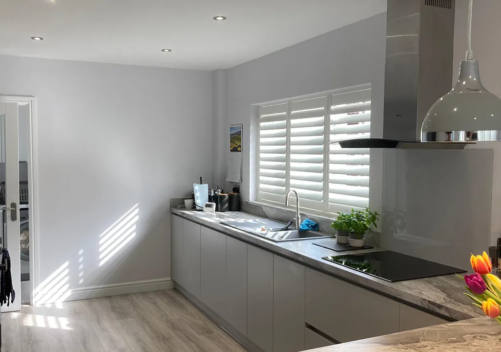 White plantation shutters on a window above the sink in a modern grey kitchen