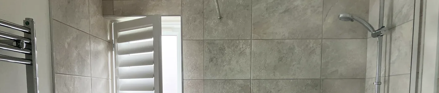 A bathroom shower alongside open shutters