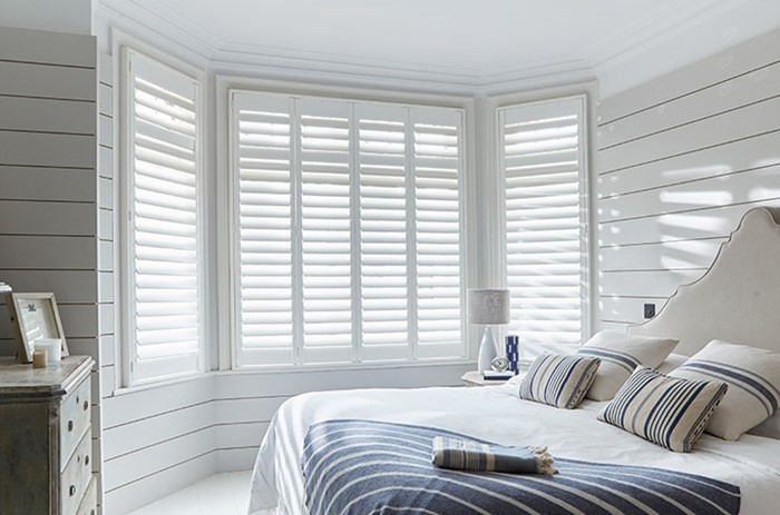 A bedroom with white walls and wooden shutters.