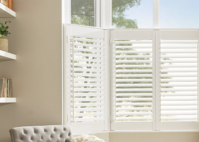 A living room with white shutters and a grey chair.
