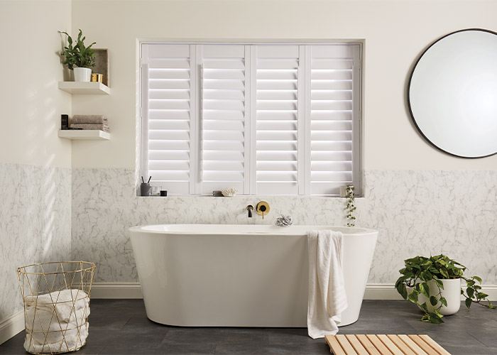 A bathroom with white shutters and a tub.