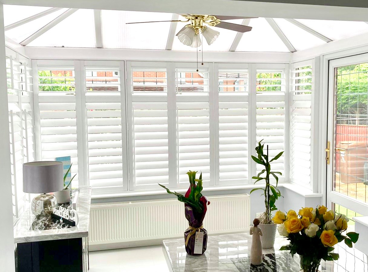 A living room with white shutters and flowers.