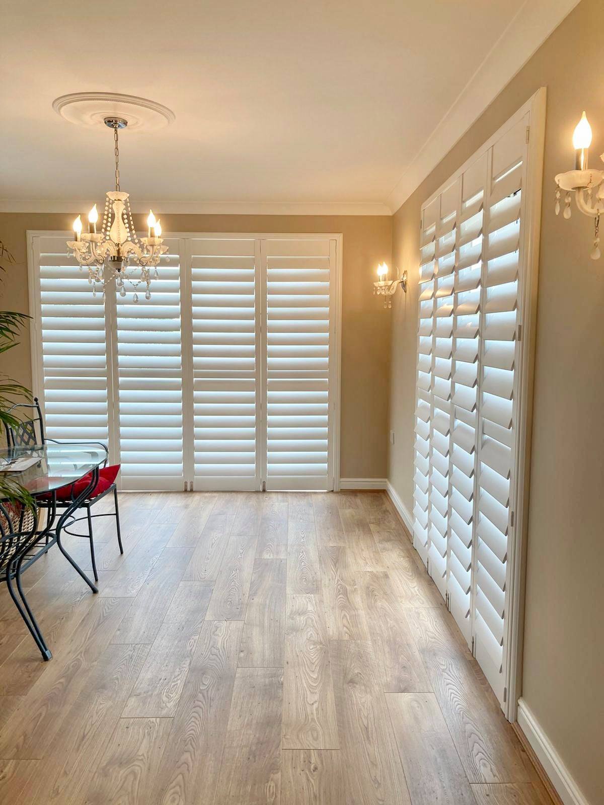 A dining room with white shutters and a chandelier.