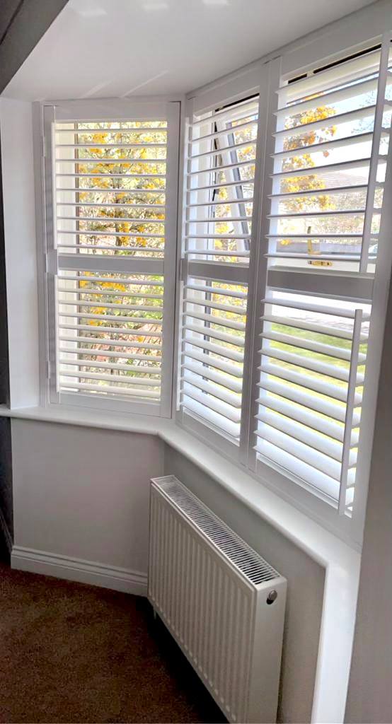 A room with white shutters and a radiator.