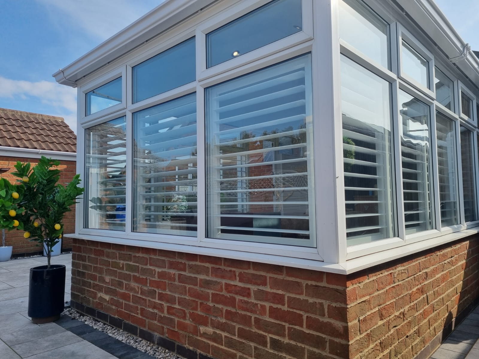 A conservatory with white shutters and a potted plant.