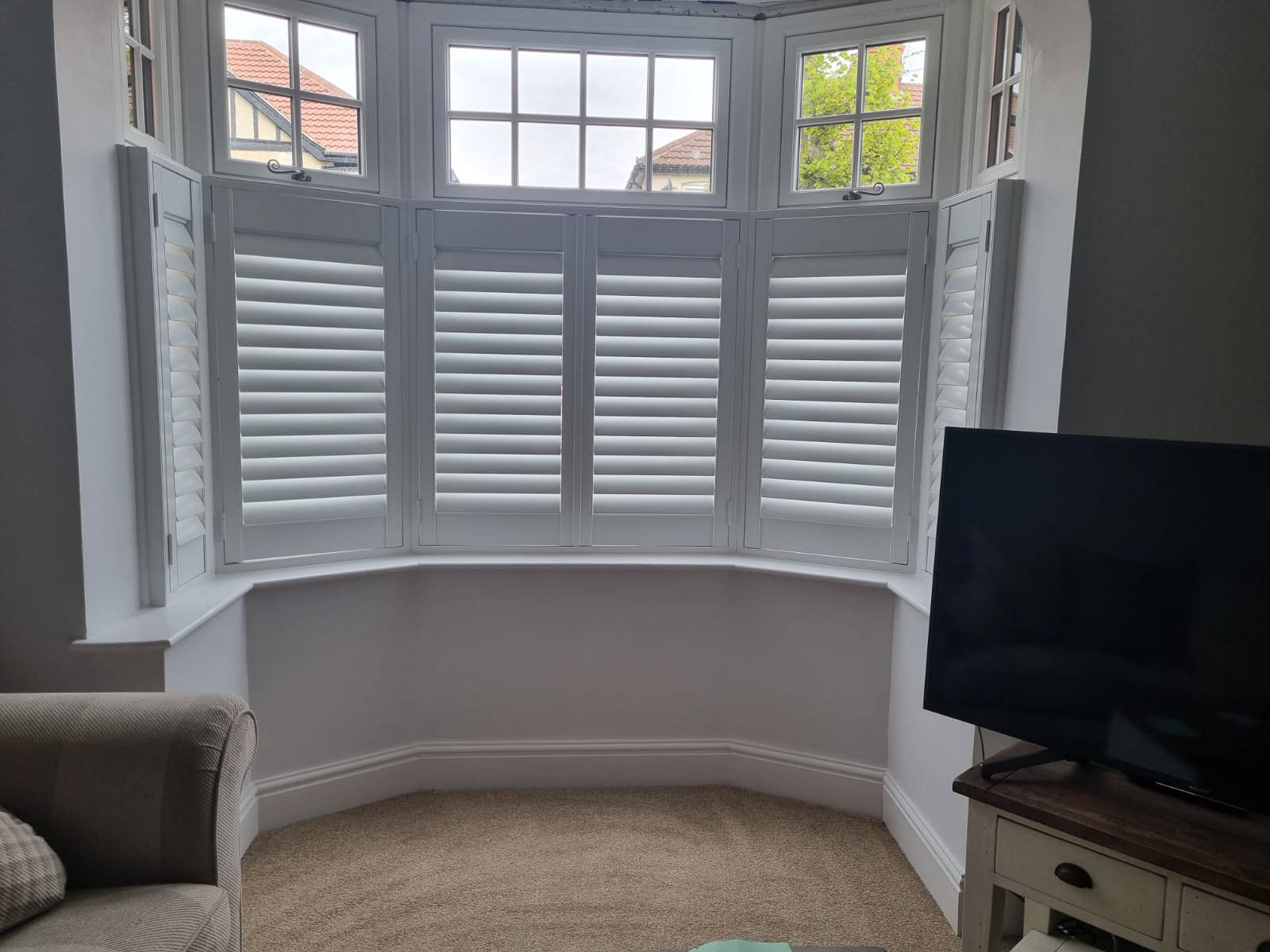 A living room with white shutters and a tv.