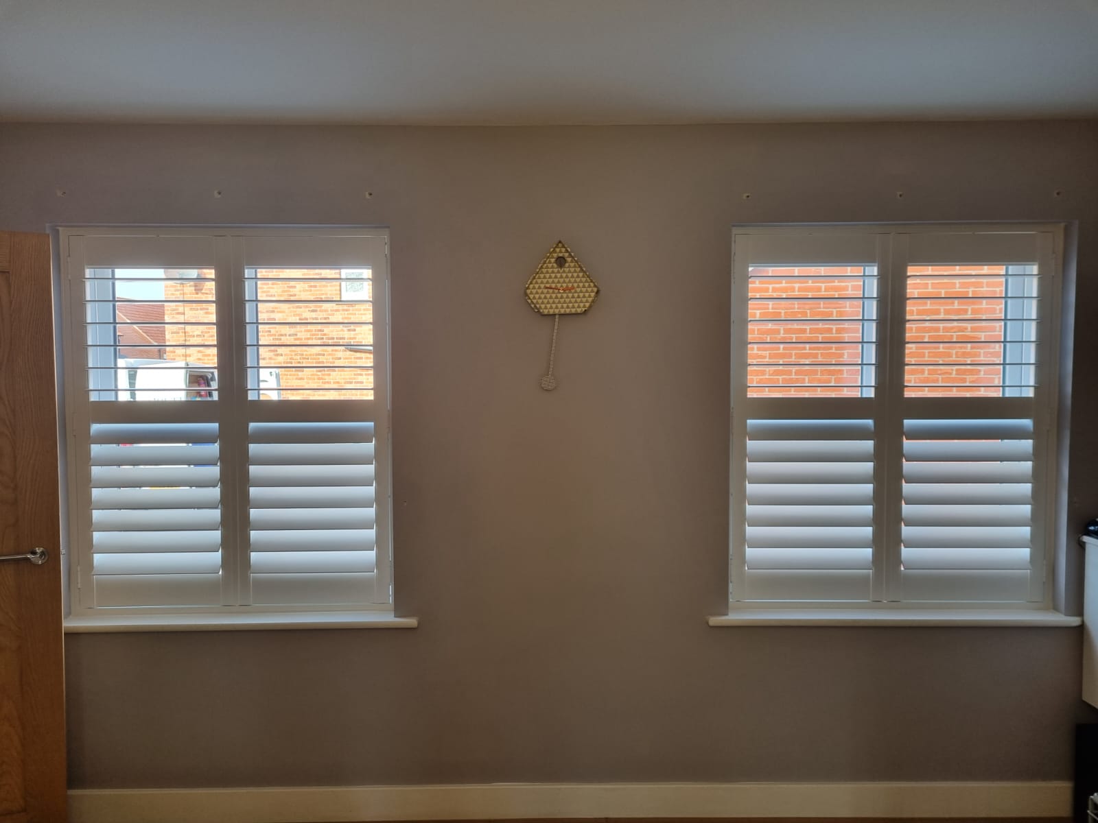 Two white shutters in a room with a clock.