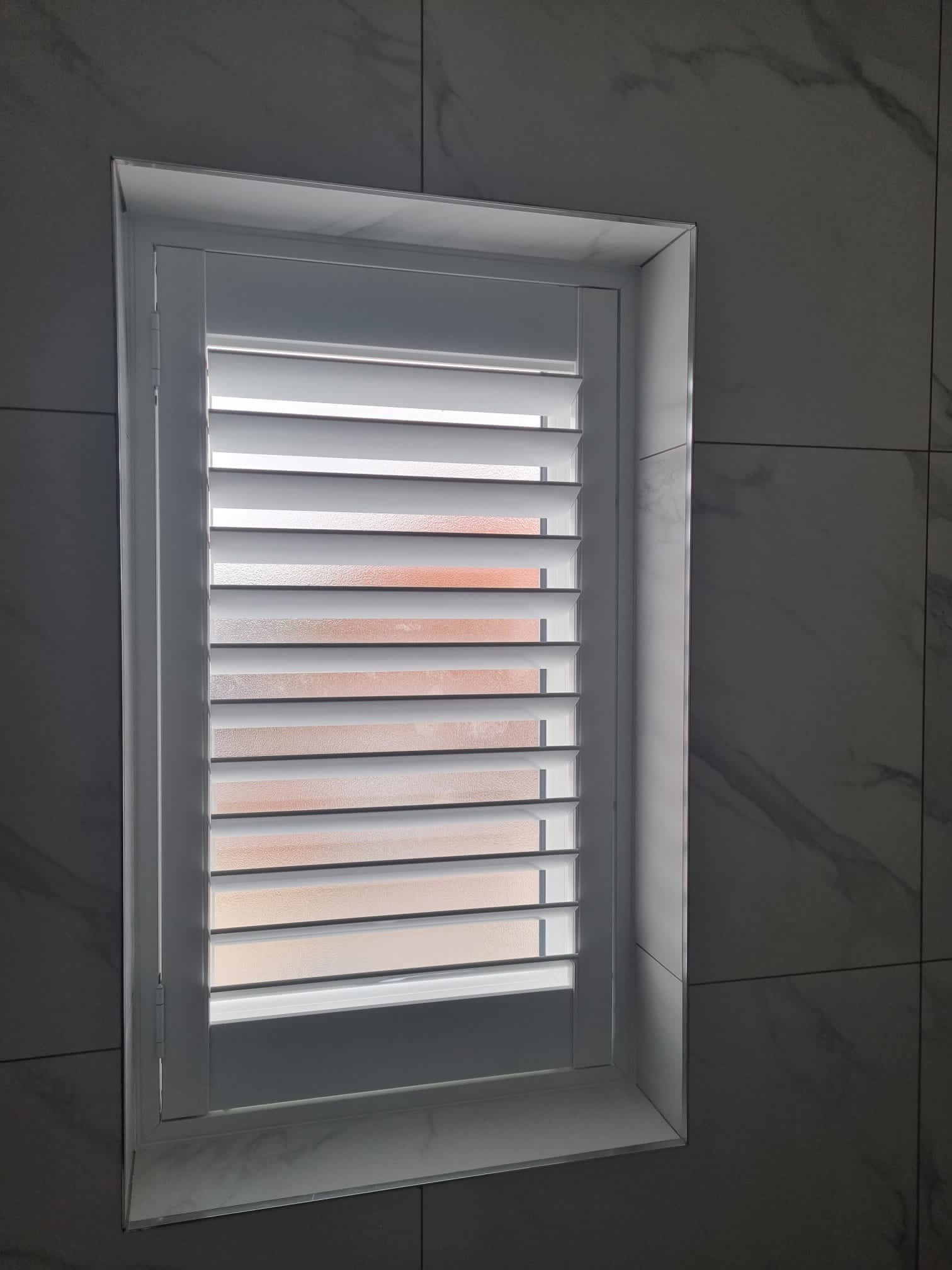 A white bathroom with white shutters and a tiled floor.