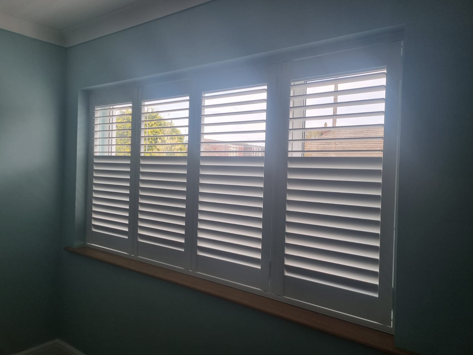 A room with white shutters in a window.