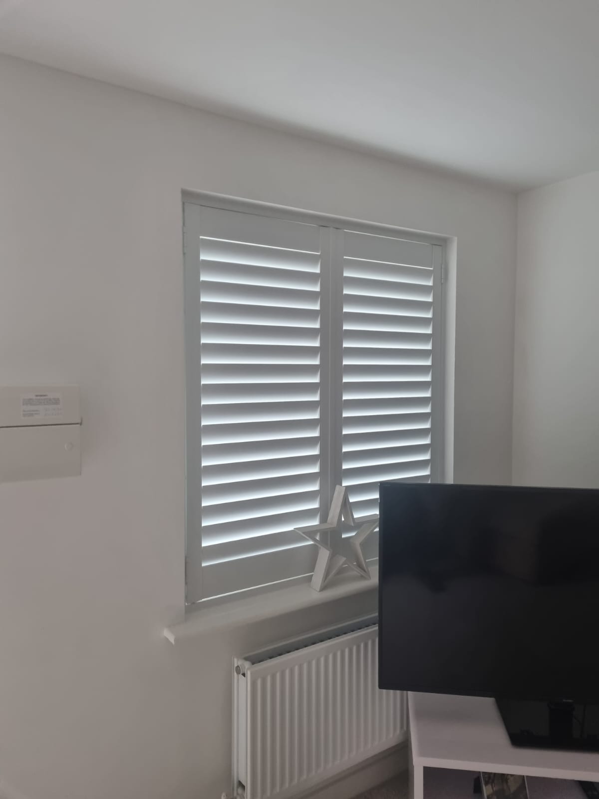 A living room with white shutters and a tv.