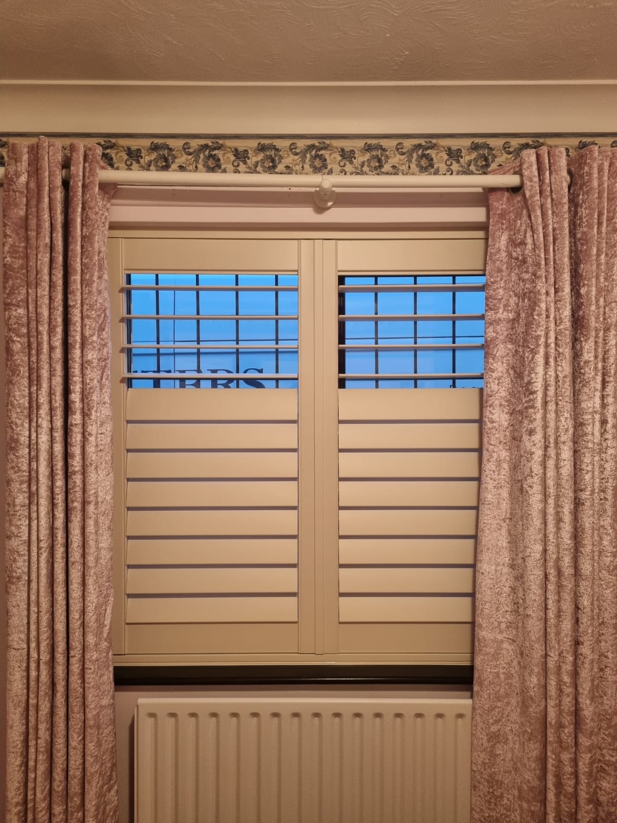 A window with shutters and curtains in a room.