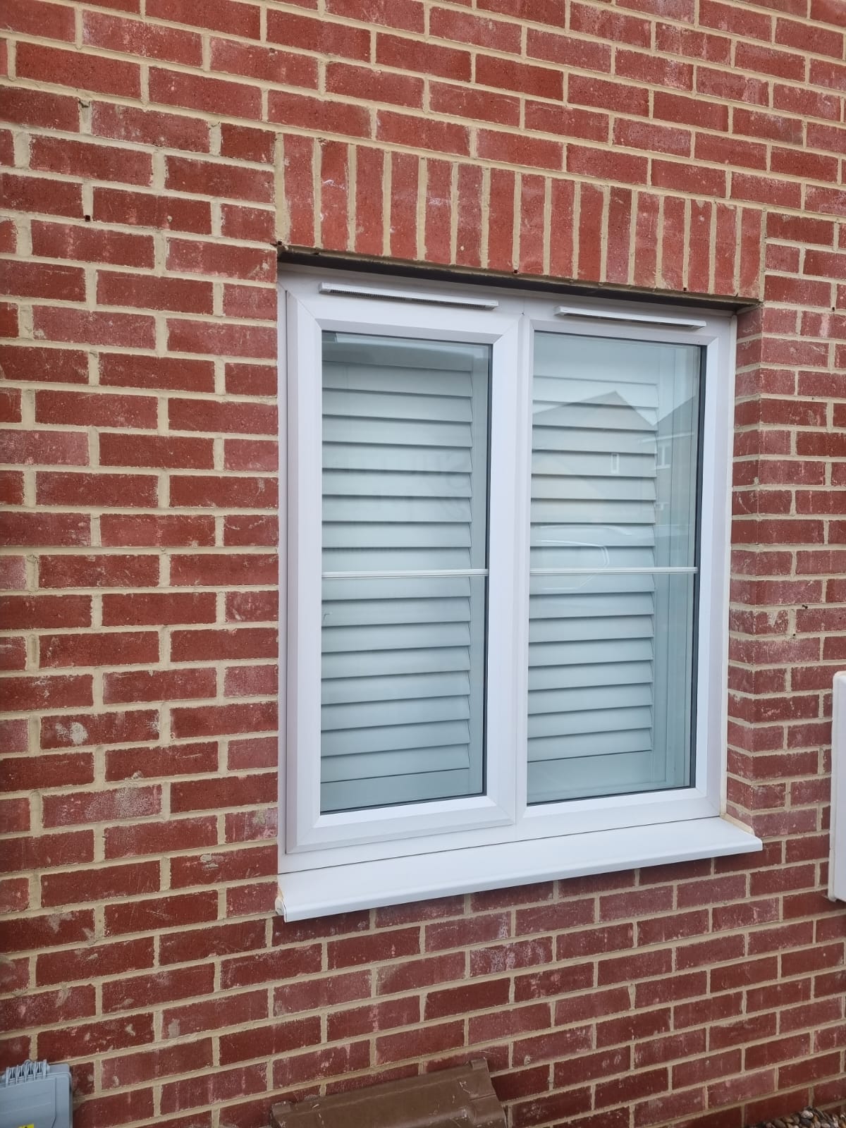 A window with white shutters on a brick wall.