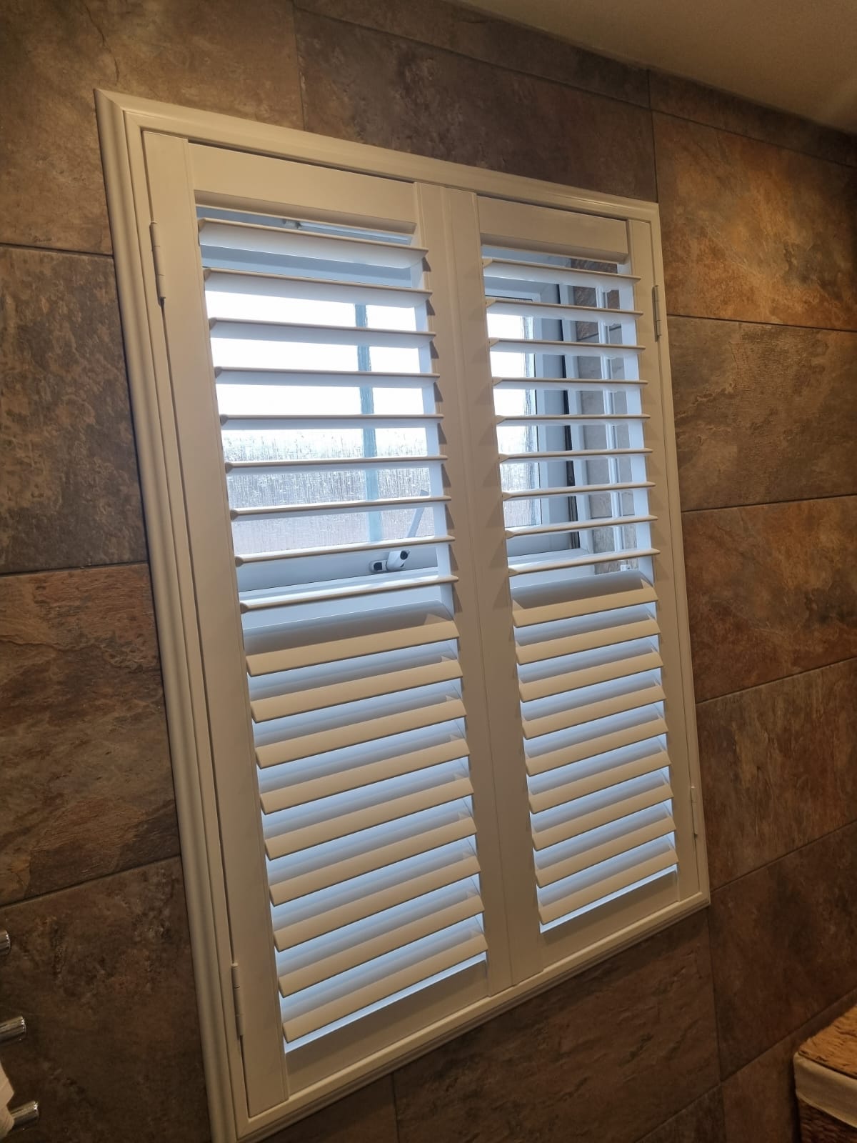 A bathroom with white shutters on a window.