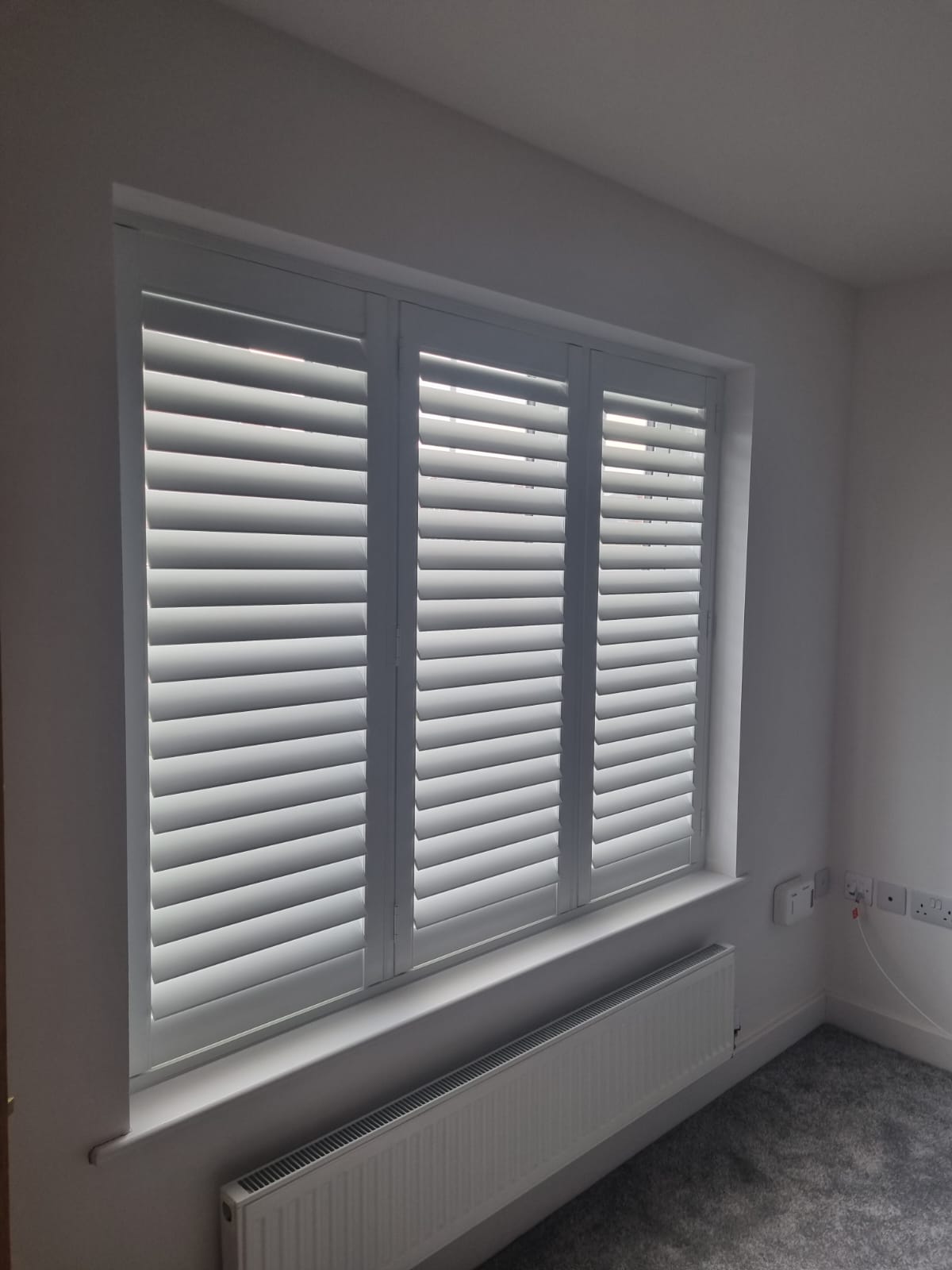 A room with white shutters and a radiator.