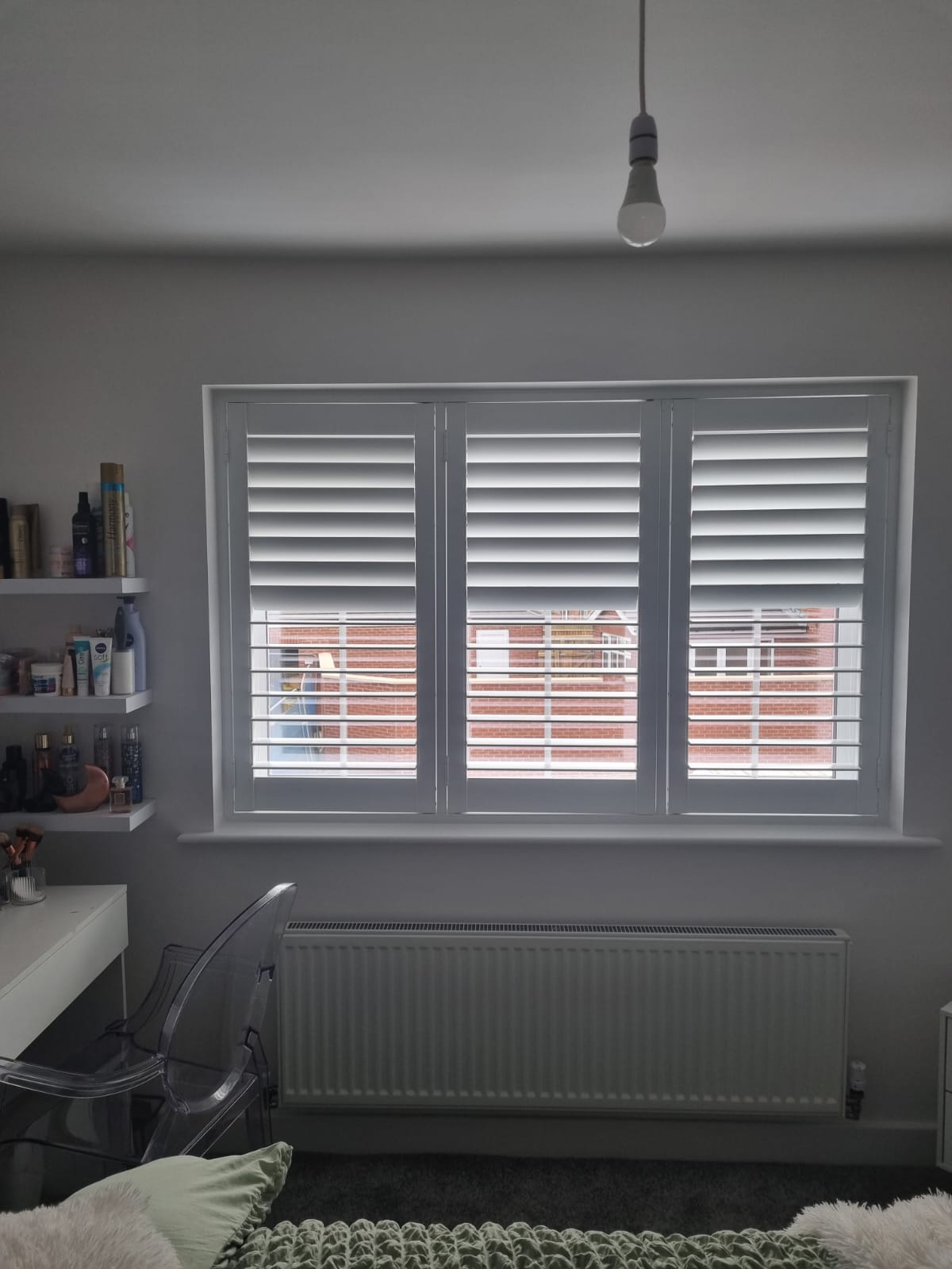 A bedroom with white shutters and a desk.