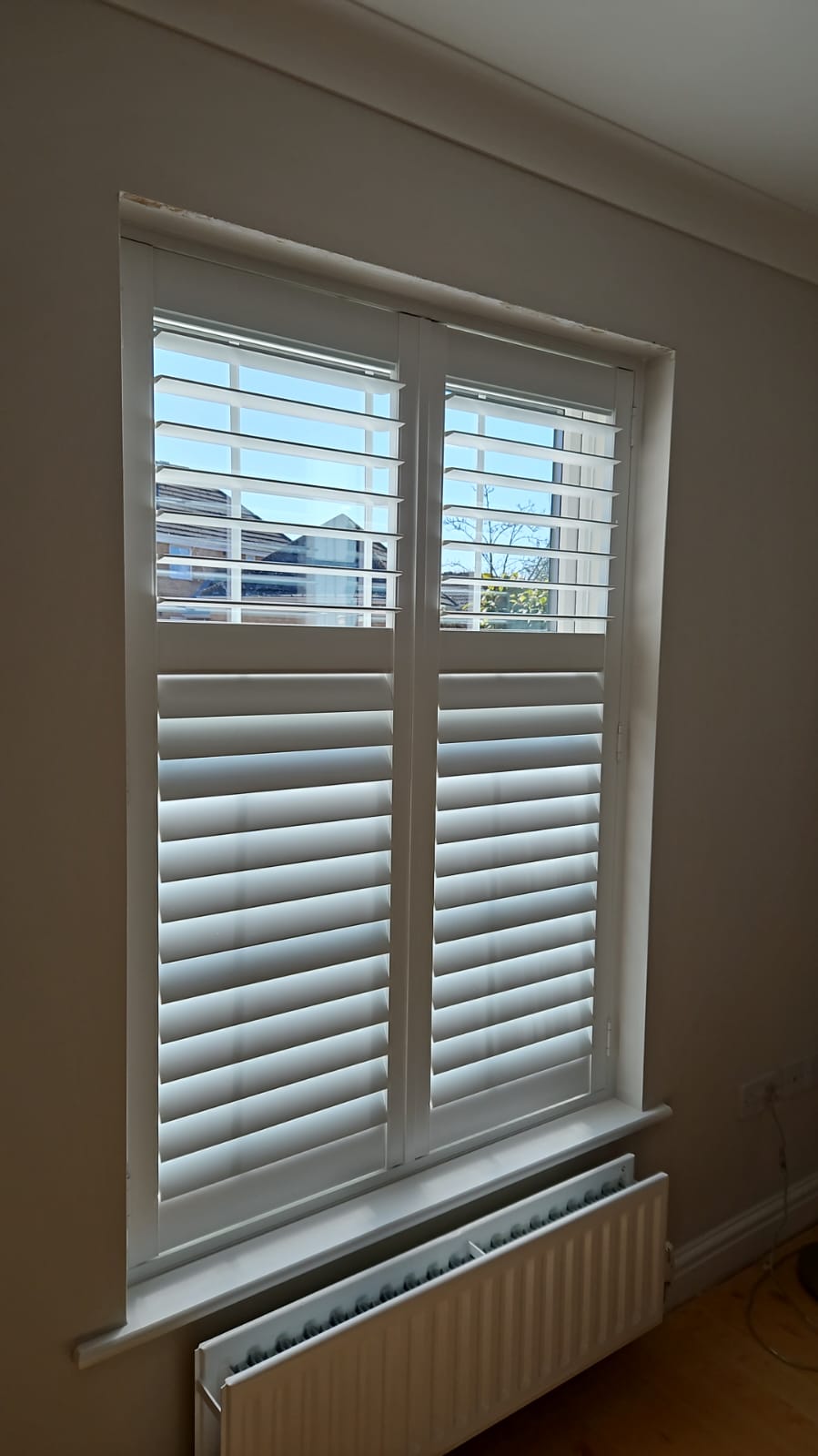 A room with white shutters and a radiator.