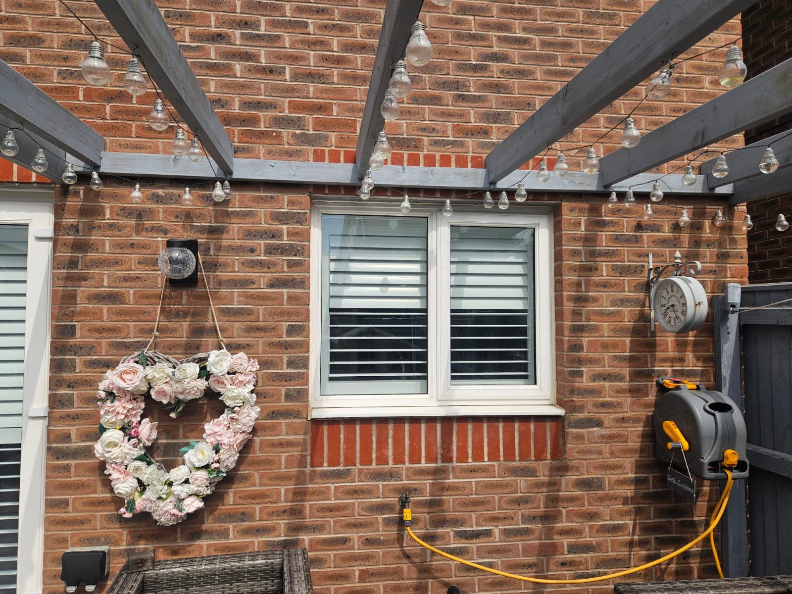 A wooden pergola with lights and flowers hanging from it.